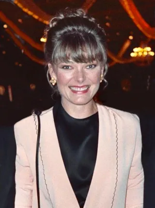 Jane Curtin smiling in a pale pink jacket over a black top, with her hair pinned up, photographed at an evening event in 1989.