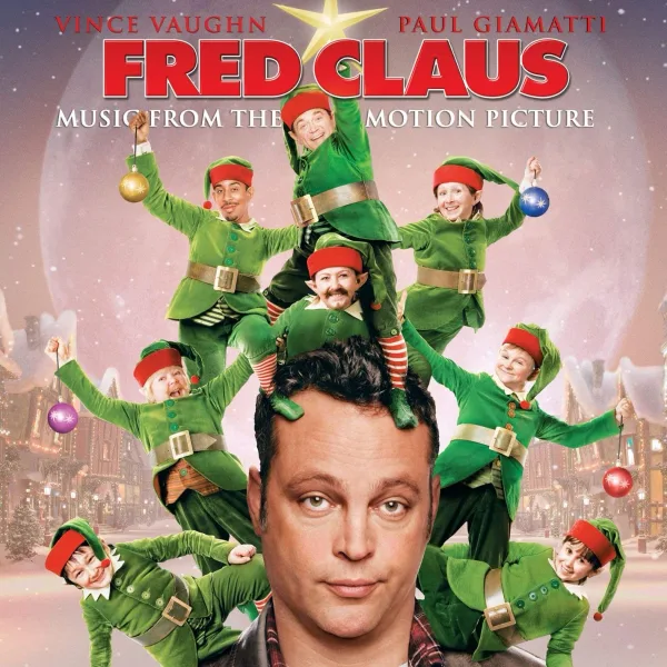 Album cover with a man's face at the bottom and a pyramid of grinning people in green and red elf outfits stacked above him against a pink snowy village and full moon.