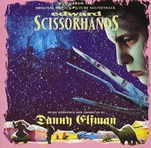 Album cover with a pale-faced man with wild dark hair and long blade-like fingers against a purple snowy sky, above a row of small pastel houses on a pink border.