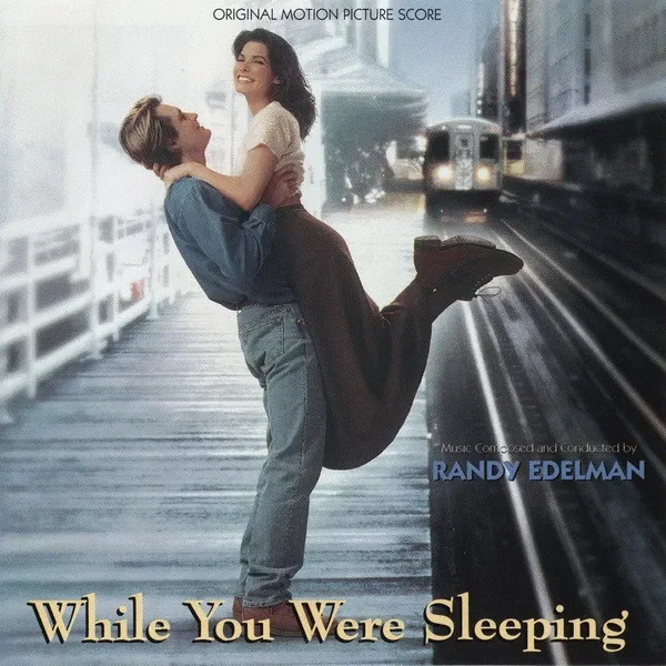 Album cover showing a man lifting a smiling woman in the air on a rainy train platform, with a train approaching and the score credit in gold lettering.