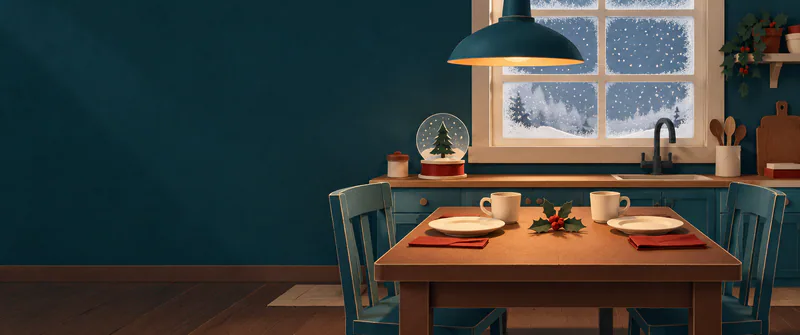 A teal paper kitchen sits in warm lamplight, with two place settings, a pine snow globe and snow beyond the frosted window.